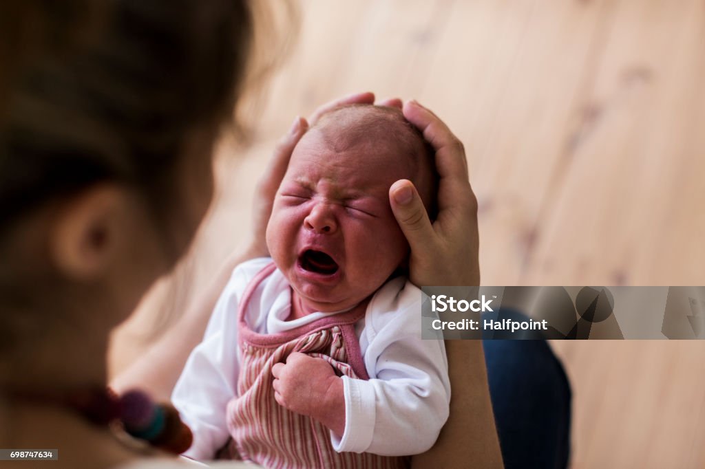 Unrecognizable mother holding crying newborn baby girl. Unrecognizable young mother at home holding her crying newborn baby girl. Crying Stock Photo