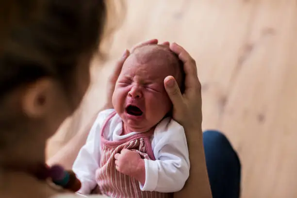 Photo of Unrecognizable mother holding crying newborn baby girl.