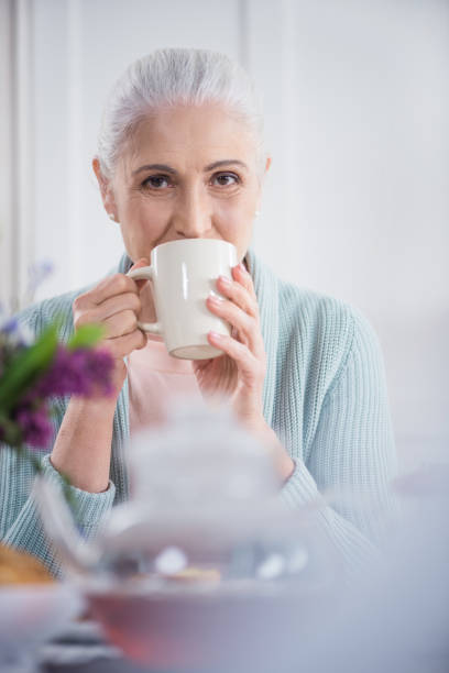 istock grey haired woman drinking coffee and looking at camera while sitting at home 698768190