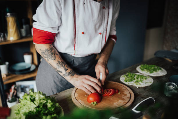 istock Tattooed chef cutting tomato on wooden board 698772614