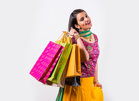 Portrait of indian young happy smiling woman with shopping bags or gift boxes in traditional wear, isolated over white background