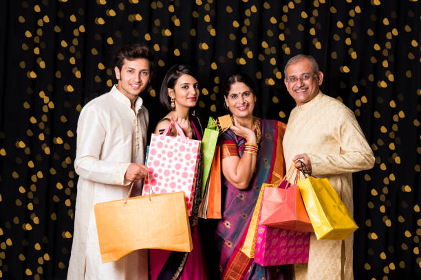 Indian family of 4 with shopping bags standing isolated over black background on diwali with bokeh, senior Indian couple in traditional wear and young kids Indian family of 4 with shopping bags standing isolated over black background on diwali with bokeh, senior Indian couple in traditional wear and young kids diwali photos stock pictures, royalty-free photos & images