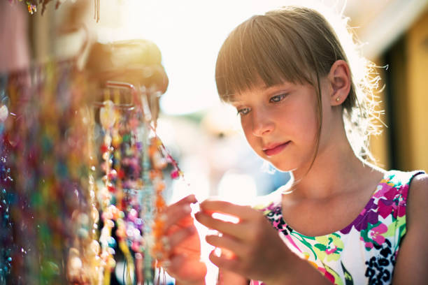 bambina che sfoglia collane colorate su uno stand di souvenir - necklace horizontal waist up outdoors foto e immagini stock