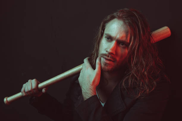 istock Confident young long haired man holding baseball bat and touching chin in studio 698829196