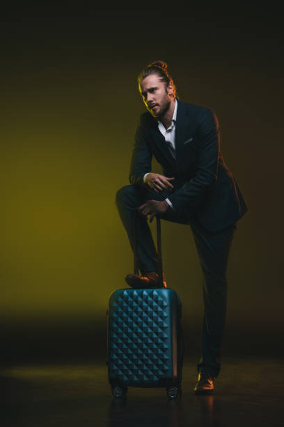 istock pensive young man in suit leaning on suitcase and looking away 698833974