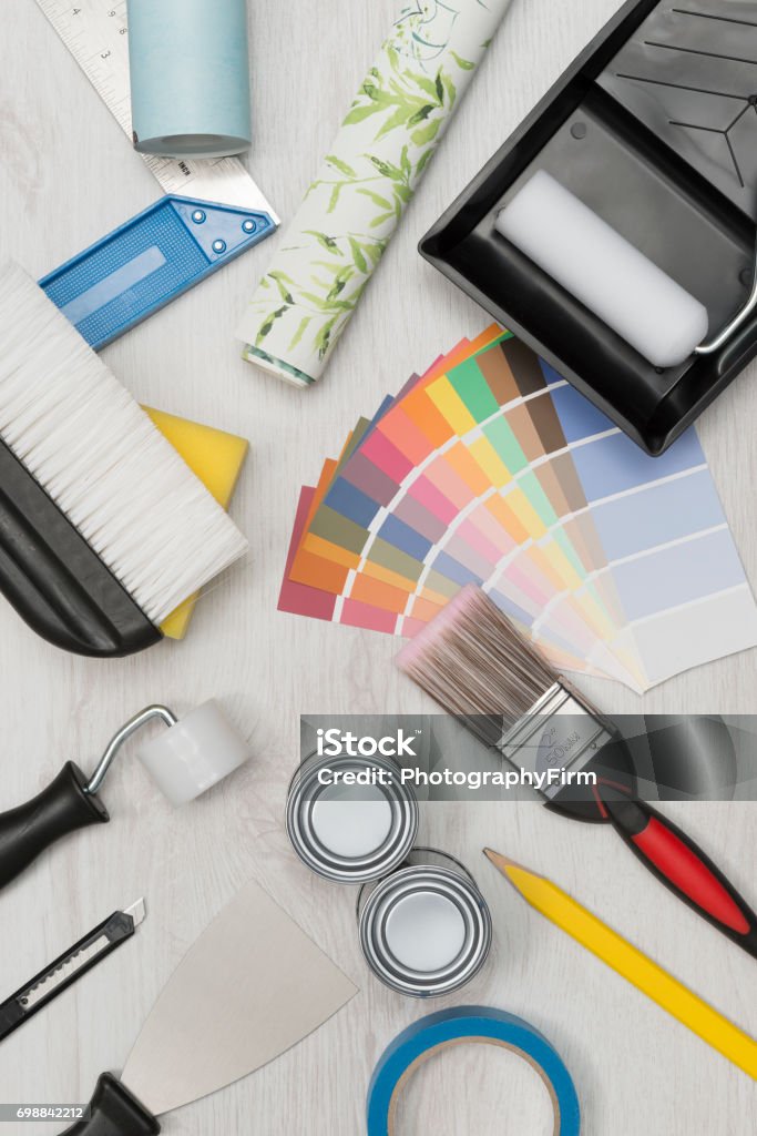 Painting Tools, Paint Swatches, and Wall Paper Roll Overhead Overhead shot of painting tools including paintbrush, roller, paint tray, foam, scraper, and paint swatches plus rolls of wall paper on wooden surface Aerial View Stock Photo