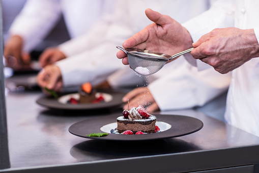Close-up of chef finishing a dessert plate with icing sugar in the kitchen