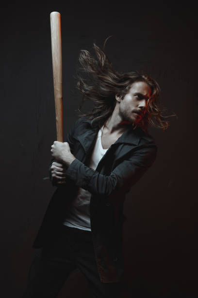 istock Young long haired man holding baseball bat ready to hit in darkness 698844902