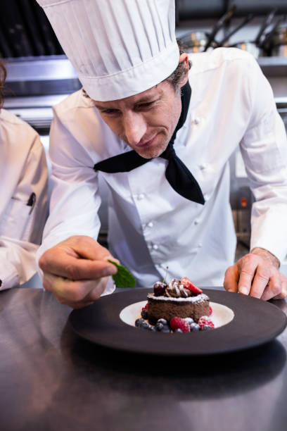 istock Male chef garnishing a dessert with a mint leaf on counter 698845292