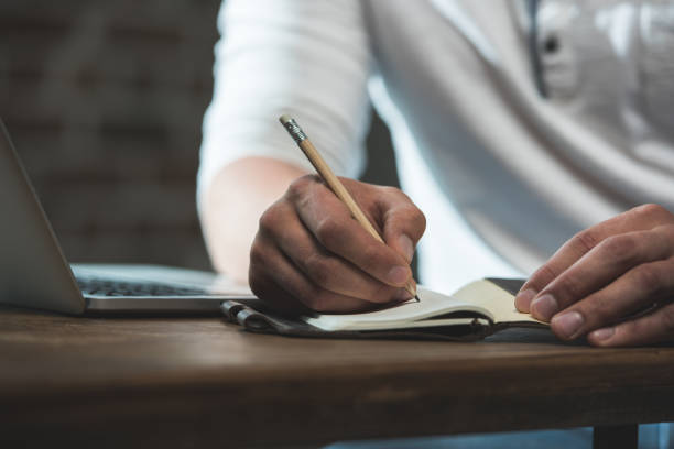 istock Cropped shot of man writing in notebook during work while sitting at the table with laptop 698853324
