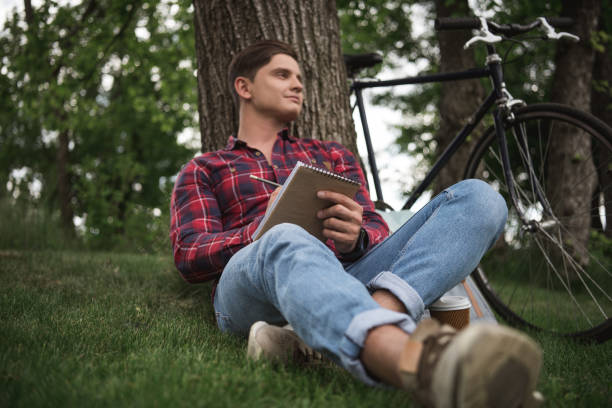 istock Young man taking notes in notebook during rest at park in summer day 698854508