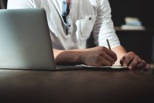 istock Cropped shot of man writing in notebook during work while sitting at the table with laptop 698854674