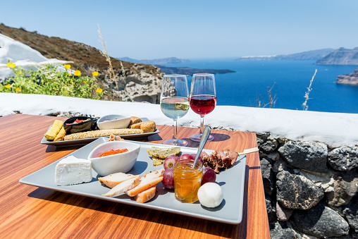 Horizontal color image of greek wines arranged on table with delicatessens for appetizer. Greek landscape and volcano in the background.