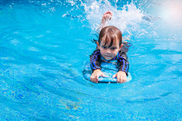 istock little boy learning to swim in pool, practicing with foam pad 698856890