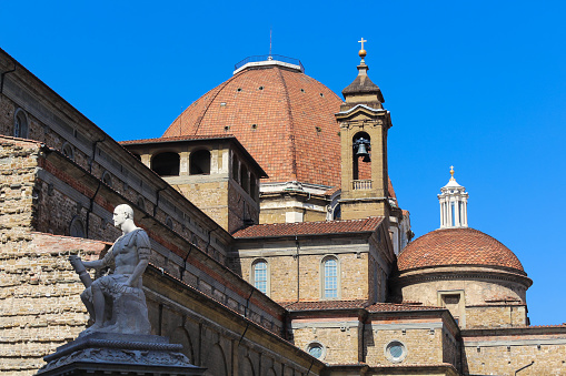 Basilica di San Lorenzo (Basilica of St Lawrence), Florence, Italy. Vivid blue clear sky is in background. Sculpture, dome and bell tower are in this close-up image.
