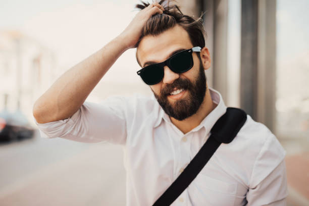 Smiling hipster in white shirt pulls fingers through his hair