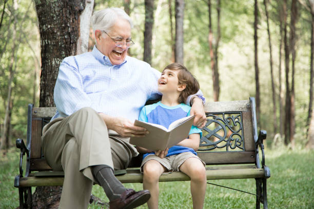 istock Grandfather and grandson reading books outdoors together. 698883984