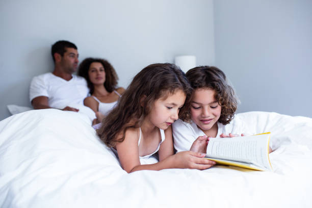 istock Brother and sister reading book together on bed 698892306