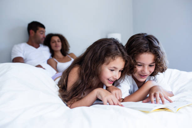 istock Brother and sister reading book together on bed 698892418