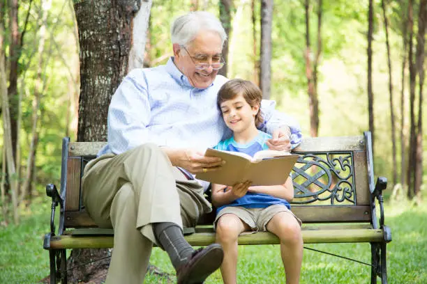 Photo of Grandfather and grandson reading books outdoors together.