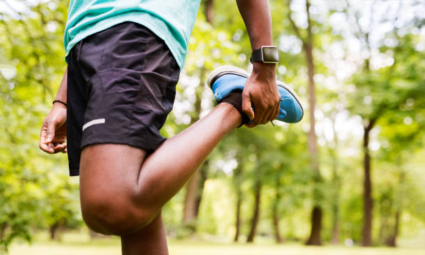 uomo afro-americano irriconoscibile nel parco che allunga le gambe. - pantaloncini da corsa foto e immagini stock