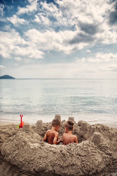 Two little boys sitting in a sandcastle on the beach