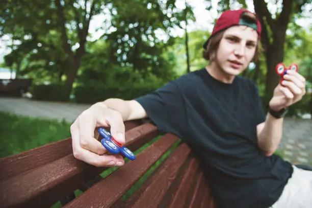 Hipster in a cap sits on a bench and spins a fidget-spinner