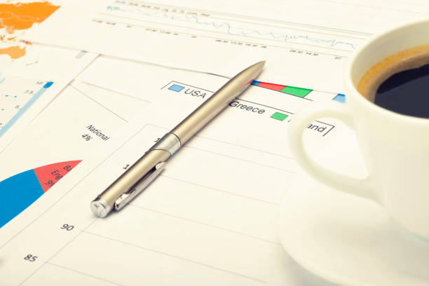 istock Coffee cup and pen over financial charts. Filtered image: cross processed vintage effect. 698940880