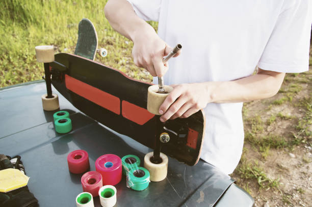 A close-up of a young guy changes his wheels on his longboard and adjusts the suspension stock photo
