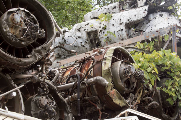 Engines and hull of wrecked airplane with weeds in junkyard.