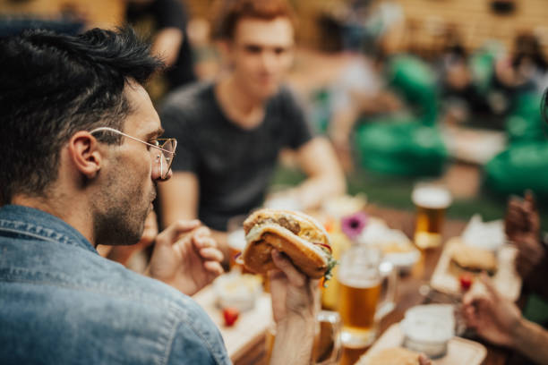 istock Man with glasses at the pub holding a burger 699124920