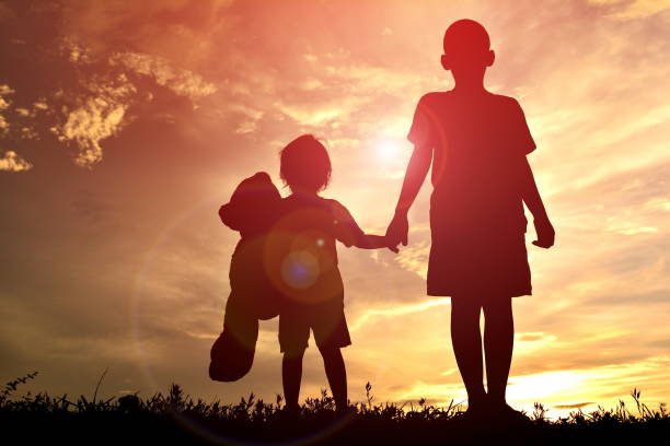 istock Low Angle View Of Silhouette Children Holding Hands While Standing Against Sky During Sunset 699174315