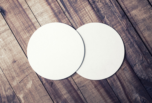 Photo of two blank white beer coasters and coffee beans on wood table background. Blank template for your design. Top view.