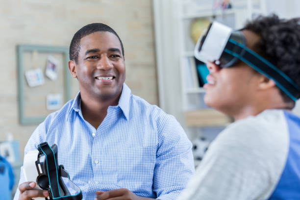 istock Father smiles while his son wears virtual reality goggles 699250996