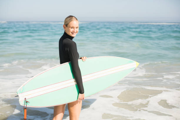 istock Woman in wetsuit holding a surfboard on the beach 699281434