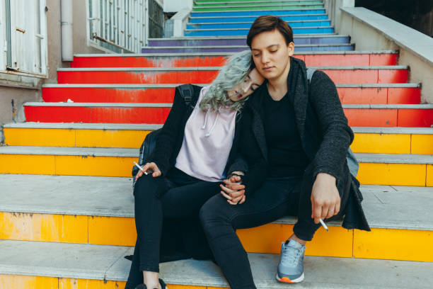 Sad urban lesbian couple enjoy Same sex young female real couple hanging out and embracing on colorful stairs in Istanbul. Looking sadly with cigarettes sad gay stock pictures, royalty-free photos & images