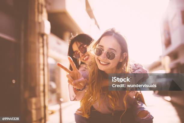 Young Woman On Piggyback Ride Doing The Peace Sign Stock Photo - Download Image Now - Friendship, Teenager, Teenage Girls