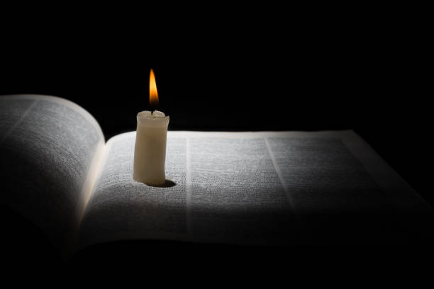 istock Burning candle on opened book on black background 699509098