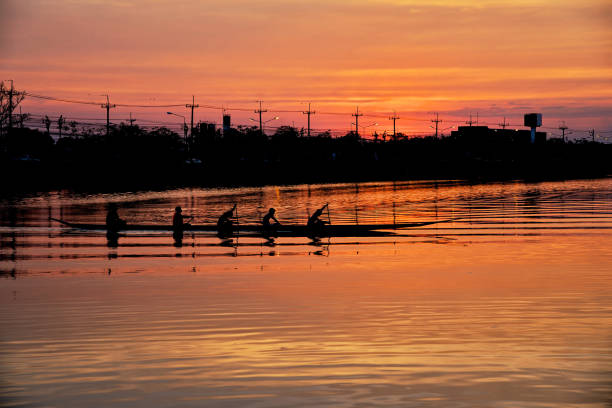 Team work of young men in a row boat silhouetted at sunset