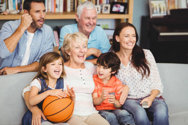 lächelnde familie beobachten basketball-match - senior women electronics people remote control stock-fotos und bilder