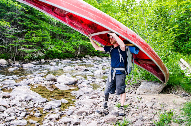 Man, seen from side, with prosthetic leg carrying his canoe and standing by the river  during a summer day