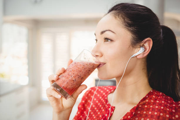 Woman drinking fruit juice while listening to music at home