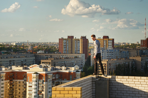 A lone roofer walks along the edge of the roof fence on a high-rise building. Courage and adrenaline. Against the backdrop of the cityscape.