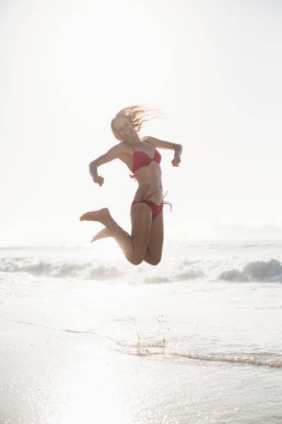 istock Excited woman in bikini jumping on the beach 699713046