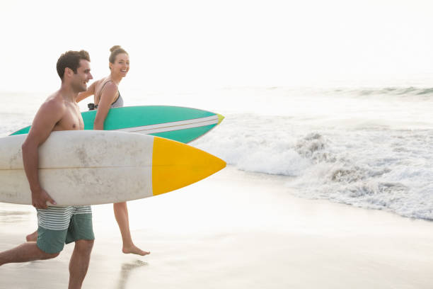 coppia con tavola da surf in esecuzione sulla spiaggia - men beach running shirtless foto e immagini stock