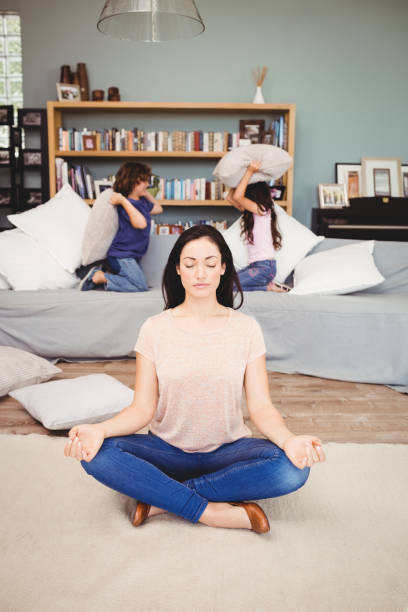 istock Woman meditating on carpet while children playing in background 699753358
