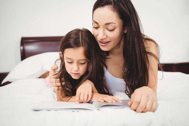 istock Daughter reading book with mother on bed 699784194