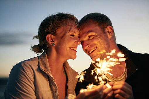 Shot of a happy young couple playing with sparklers on the beach at sunset