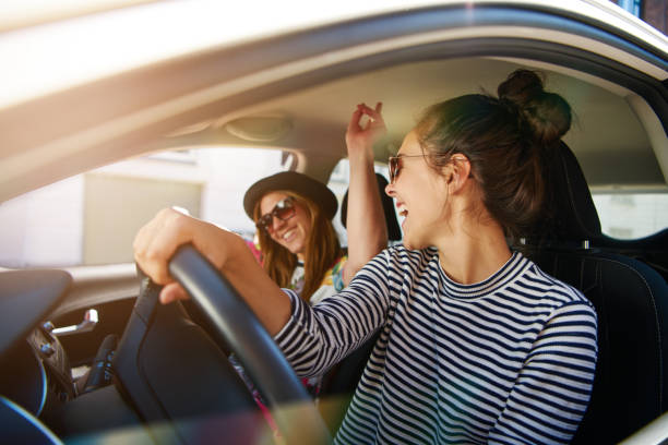 dos mujeres jóvenes que se divierten conduciendo por una calle - cantar fotografías e imágenes de stock