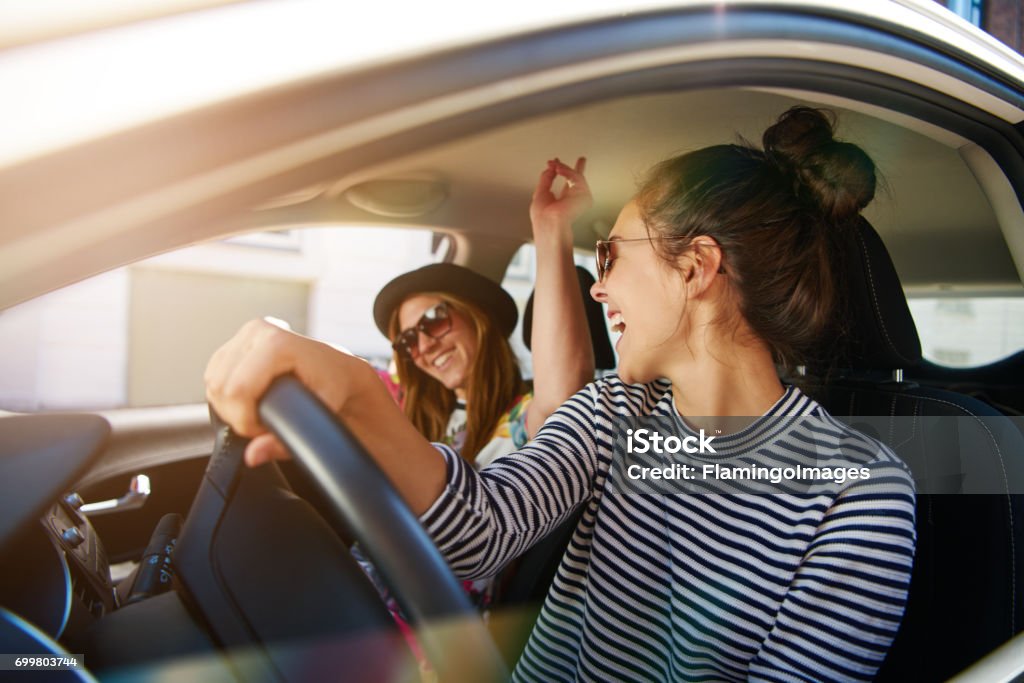 Two young women having fun driving along a street Two young women having fun driving along the street laughing and joking with the driver distracted looking at her passenger Car Stock Photo